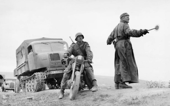 Operación Ciudadela. Kursk, Unión Soviética. Soldado dirigiendo el tránsito. En primer plano, se ve una motocicleta para terreno fangoso y en la parte posterior un vehículo de transporte Ost (RSO). This file is licensed under the Creative Commons Attribution-Share Alike 3.0 Germany license. Attribution: Bundesarchiv, Bild 101I-022-2925-17 / Wolff/Altvater / CC-BY-SA 3.0